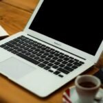 A laptop, a notebook and a cup of coffee on a wooden desk