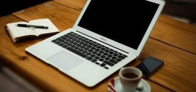 A laptop, a notebook and a cup of coffee on a wooden desk